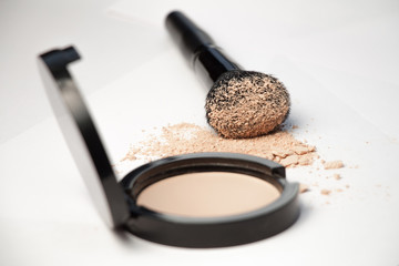 black cosmetic brush and puff-box of powder on a white background 