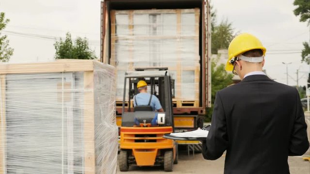Loading cargo on a container with a forklift under the supervision of quality inspector wearing a suit
