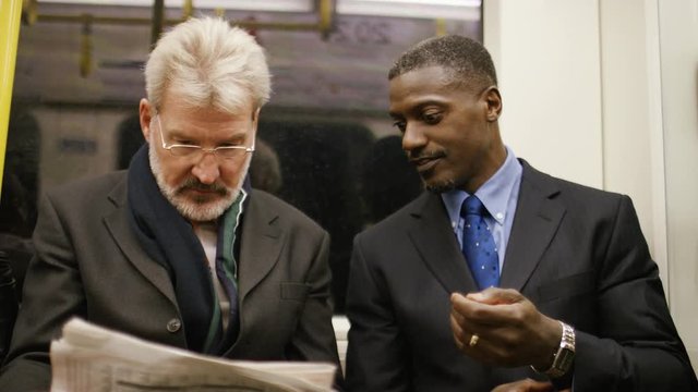 4K Two businessmen discussing a newspaper article on a train as they commute