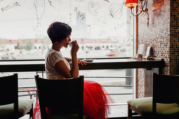 Woman in vintage cafe sitting and drinking coffee by the window looking the charming city street....