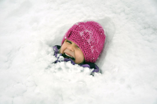 Liten tjej som gömmer sig i all snö som anlänt. Hon leker glatt i varm overall och rosa mössa.  