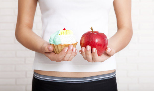 Woman chooses to eat an apple or cake. Woman holding an apple and a cake. Concept of natural food