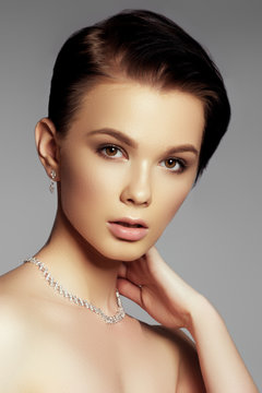 Elegant fashionable woman with jewelry. Beautiful woman with a diamond necklace. Beauty young model with a diamond pendant on a gray background. Jewellery and accessories. Beauty and fashion concept