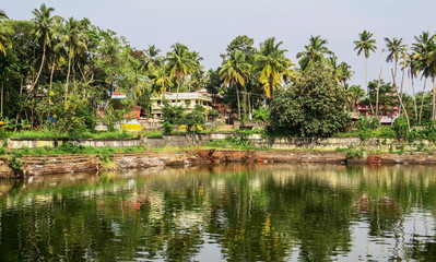 Fototapeta na wymiar Old small pond ritual - kunda in Varkala, Kerala, on the background of palm trees, greenery, and residential villas in the distance. South India.