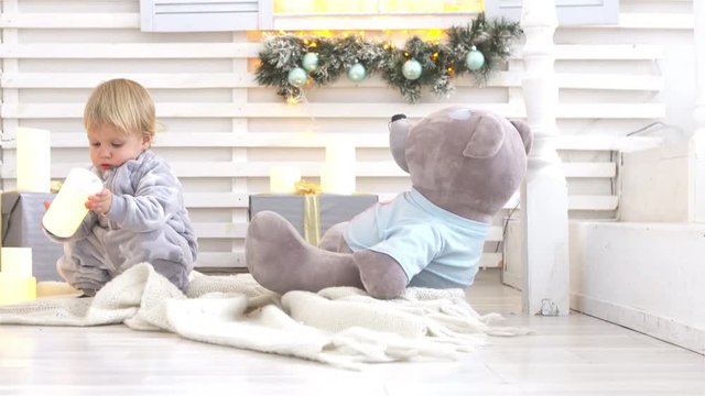 Year-old baby sits near a window with christmas decorations and play with big teddy bear toy. New Year concept