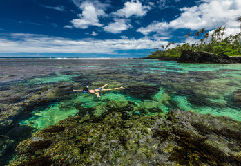 Young woman snorkeling over coral reef on a tropical island