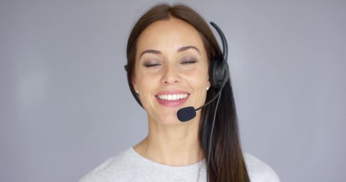 Adorable and beautiful female call center agent speaking with someone on headset. She has smile on her face. Isolated on gray.