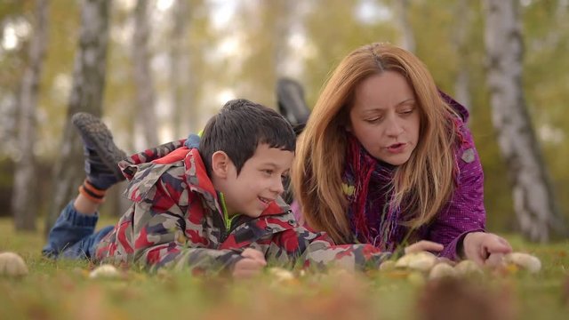 Mother and young son lying on the grass and watching and talking about mushrooms in autumn