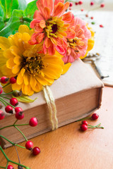 Old book with orange zinnia, key and autumn berries