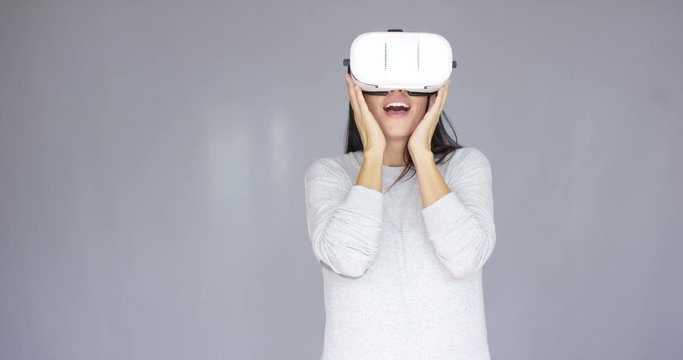 Excited woman watching something on her 3d virtual reality helmet. She is full of expression on her face. Isolated on gray background.