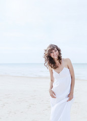 Fototapeta na wymiar Beautiful woman in a white dress on the ocean coast. Happy girl on the beach, the wind fluttering hair. Beach vacation.