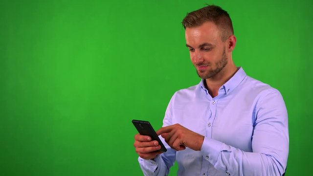 young handsome business man works (typing) on smartphone - green screen - studio