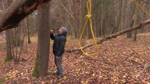 Depressed man near tree with gallows noose