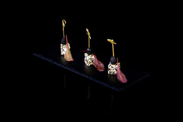 canape with cheese, sesame and olives on black background with r