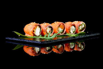 Roll of salmon stuffed with cheese on a black background with re