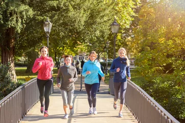 Foto auf Acrylglas Joggen Vier junge Frauen joggen über die Brücke