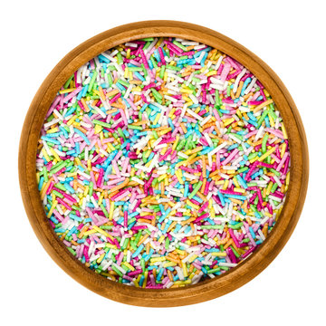 Colorful sugar sprinkles for food decorations in wooden bowl on white background. Multi colored bakery decoration ingredient, used for cakes and cookies. Isolated macro food photo close up from above.