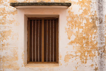Fototapeta premium Vintage window on old wall - An old window with rusted protective mesh and rods on a old wall.