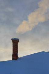 Chimney smoke rising from a snow covered house.