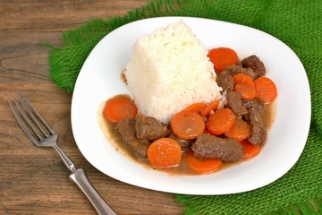 Czech meal from beef meat and carrot with rice on white plate on green gunny cloth on dark wooden background