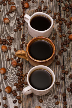 Three cups of coffee, hazelnuts and cocoa beans on wooden background
