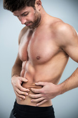 Muscular man pinching a fat on his abdomen
