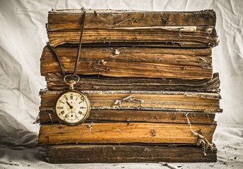 Pile of old dusty books with broken pocket watch on white cloth
