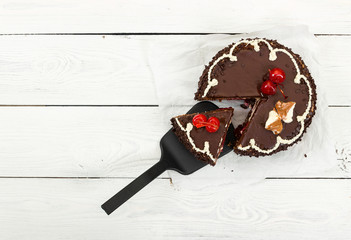Chocolate cake with cherry on wooden background.