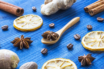 star anise, dried lemon, cinnamon, ginger and coffee beans with wooden spoon on blue wooden table