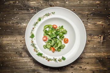 fresh greens with tomato in a beautiful white bowl on wooden background