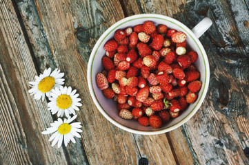 Strawberries in a cup on a wooden background and chamomile