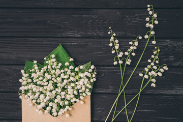 Lily of the valley on black wooden background. Top view of lily of the valley bouquet in craft envelope. Lily of the valley with copy space.