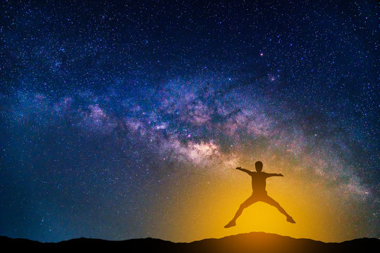 Landscape with Milky way galaxy. Night sky with stars and silhouette jumping man on the mountain.