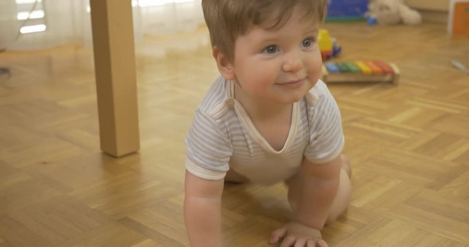 Tracking shot of adorable baby boy crawling on wooden floor. 
