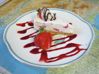 Slice of Strawberry Cheesecake, drizzled on plate, on top of a map