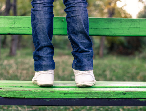 man wearing jeans and white sneakers is standing on green  bench