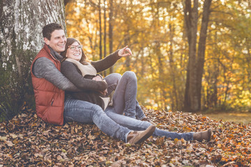Verliebtes Paar sitzt lachend unter einem Baum im Herbst