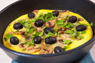 omelet with mushrooms, and olives in a frying pan