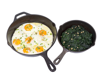 Fried eggs and sauteed spinach on cast iron skillet isolated on white background
