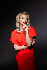 Beautiful blonde girl in red evening dress over grey background.