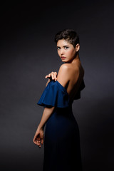 Beautiful brunette girl in evening dress posing over grey background.