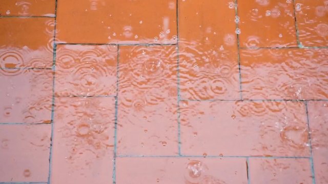 raindrops falling on terrace red floor tiles and it happens a big splash of water on heavy rain with water stream and bubbles