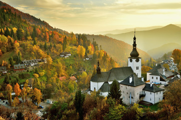 Fall in Slovakia. Old mining village. Historic church in Spania dolina. Autumn colored trees at sunset. - obrazy, fototapety, plakaty