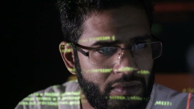 Data code reflection on programmers face. Hackers in glasses hacking programm code at night. HD.