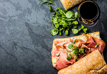 Ciabatta sandwich with jamon ham, arugula, red wine, slate background