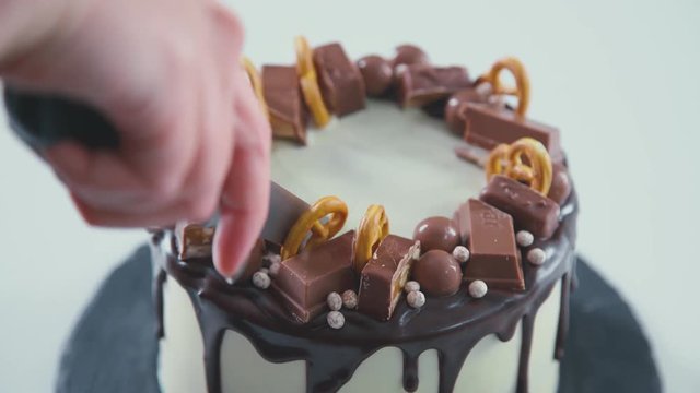 Slice of chocolate cream brownie cake topped with white chocolate. Female hands cut homemade cake. Girl makes cake, cutting shortcake into two layers. Cutting chocolate cake. Cake Rustic