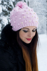 The woman poses in the winter wood in a knitted cap