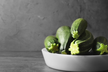 Bowl with fresh green zucchini on color background