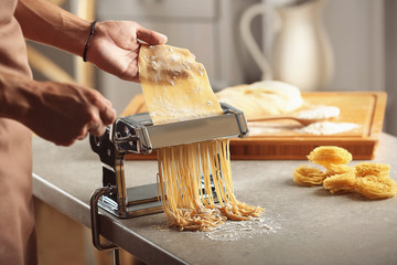 Man using pasta machine to prepare spaghetti, close up view - obrazy, fototapety, plakaty