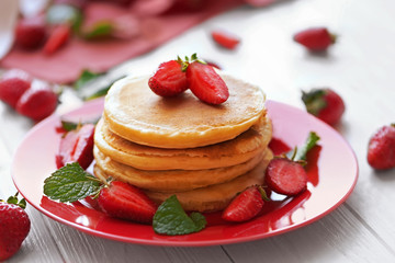 Plate with tasty pancakes and strawberries on wooden table